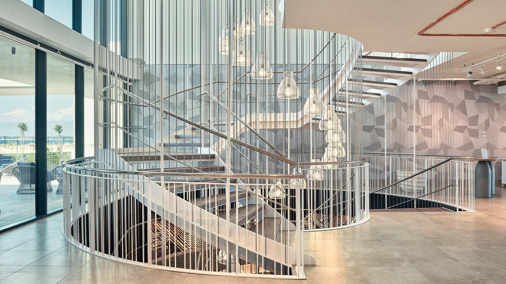 Modernes Treppenhaus mit geschwungener Metalltreppe und geometrischer Wandgestaltung in einem hellen Gebäude.