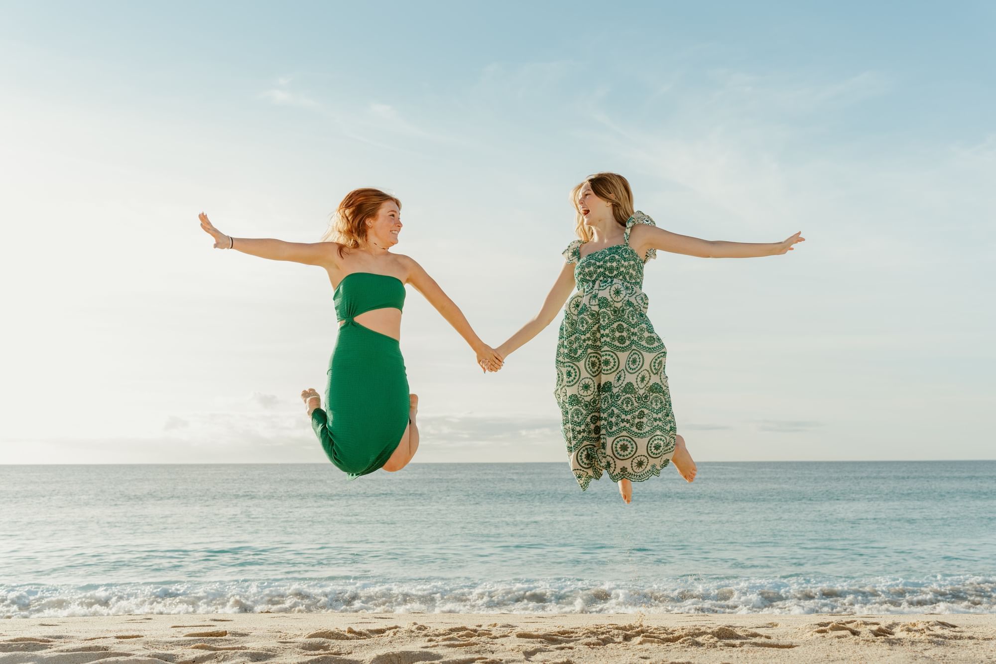 Two joyful women jumping on the beach, enjoying the ocean breeze near Marquis Los Cabos Resort