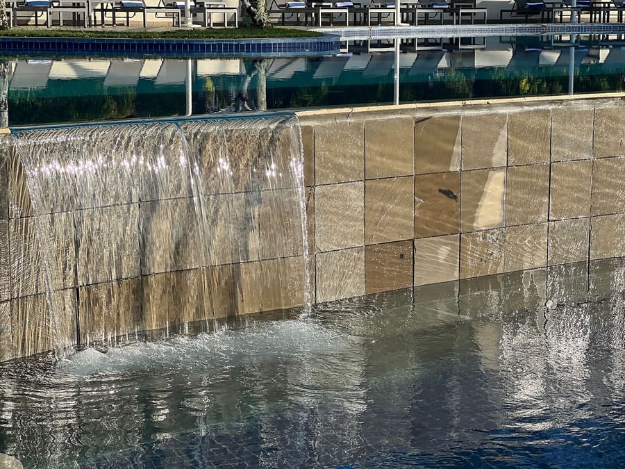 Water cascades down a tiled wall into a pool with lounge chairs at Warwick Le Lagon - Vanuatu.