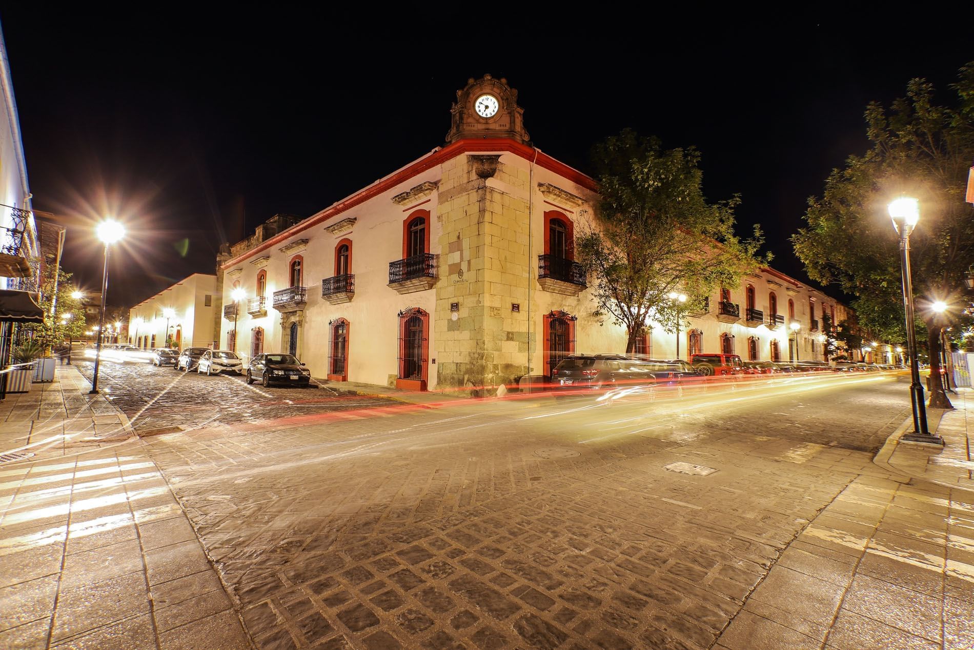 Exterior view of the Quinta Real Oaxaca with a clock tower on a cobblestone street at night, warmly lit by streetlights