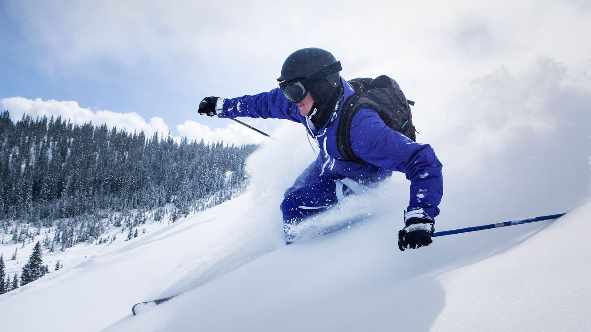 Skier slicing through deep snow surrounded by trees near Listel Whistler, a Coast Hotel