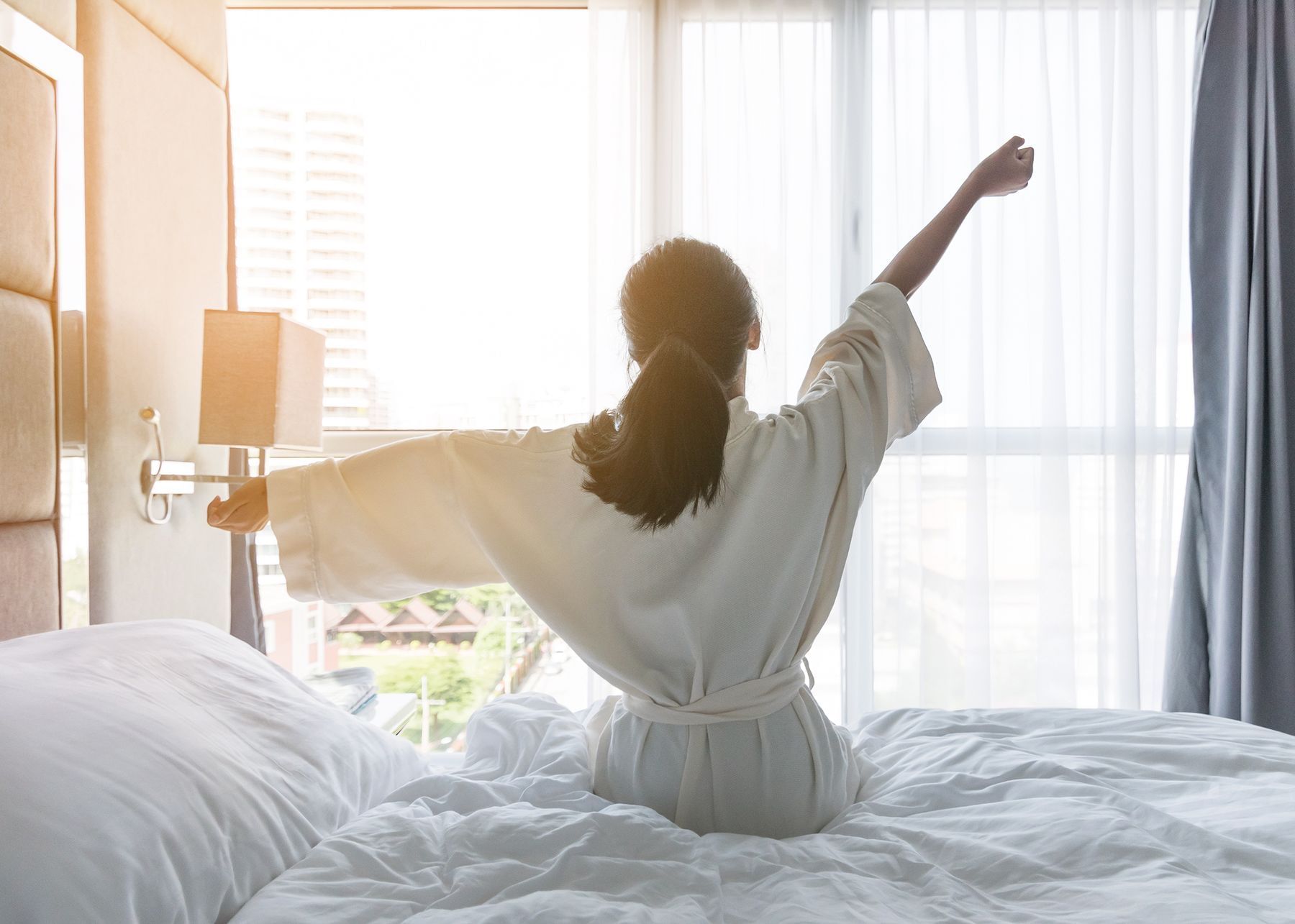 Woman in robe stretching as she rises out of bed