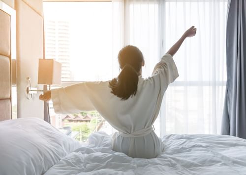 Woman in robe stretching as she gets out of bed