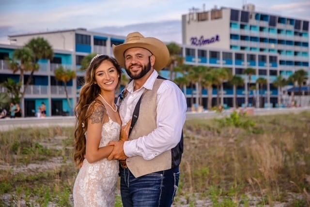 A couple in a beach setting with a large hotel building in the background.