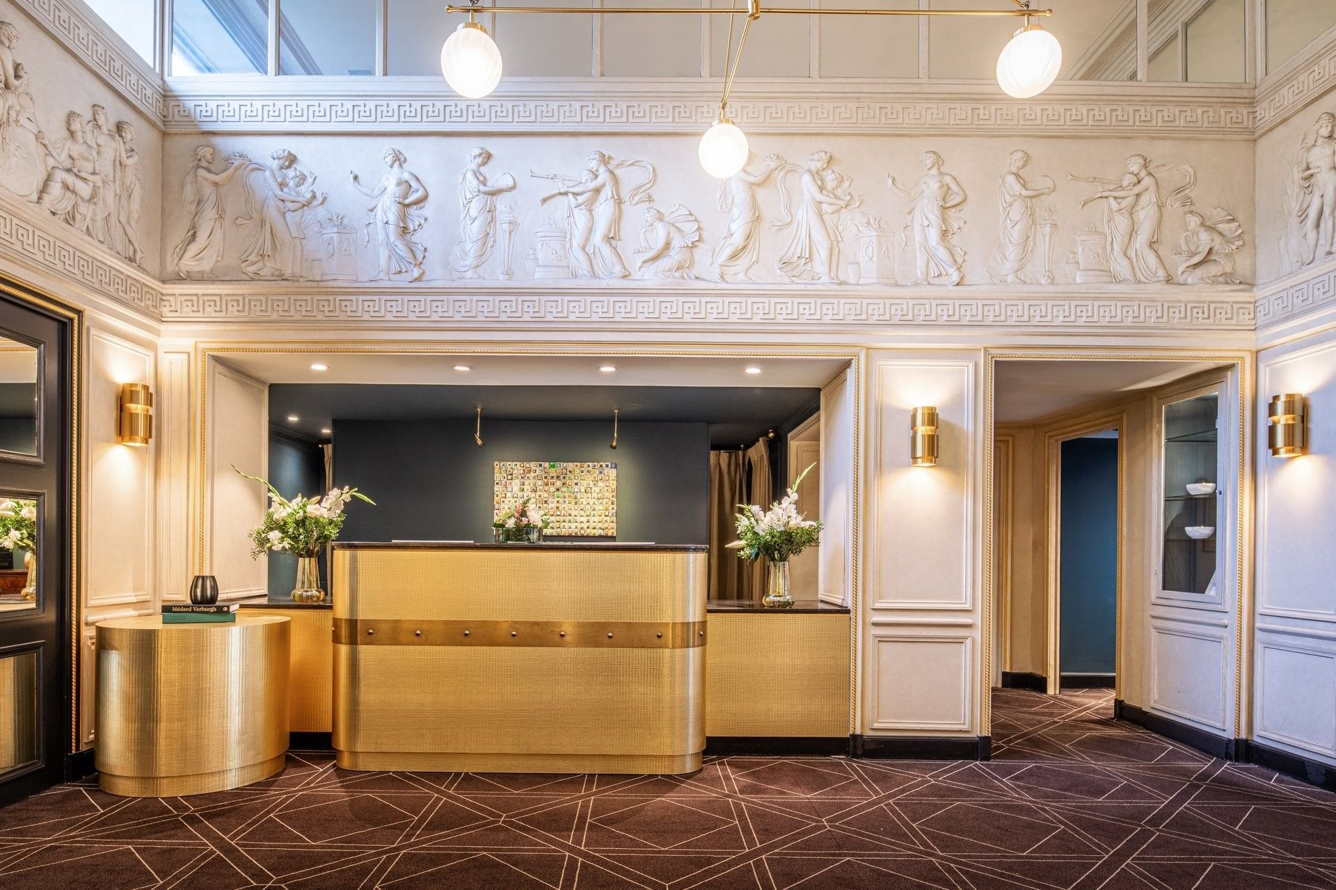 Gold textured reception desk under classical friezes and globe lights at Hotel Barsey by Warwick