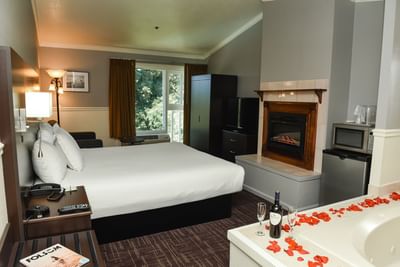 TV with fireplace facing bed by the window, and bathtub with rose petals in Superior King at Lake Natoma Inn