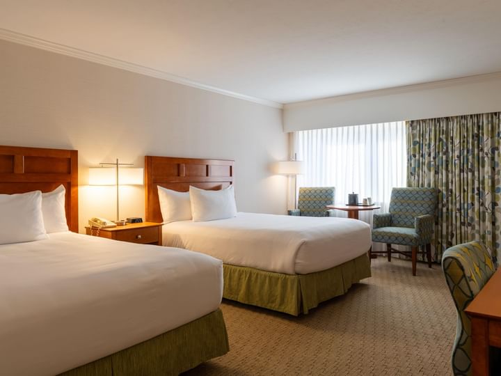 A hotel room with two beds, two chairs, and a window.