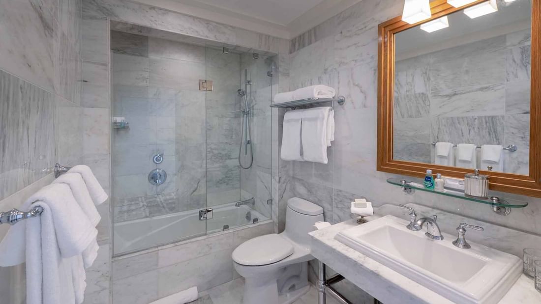 Bathroom featuring a glass-enclosed shower over a tub, and a vanity & mirror in Deluxe Queen Queen room at El Prado Hotel