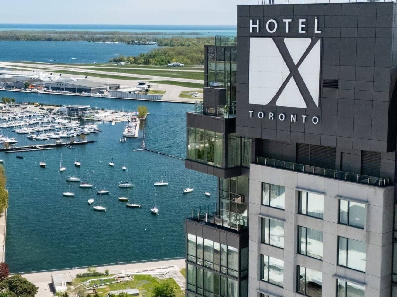 Hotel X Toronto exterior tower signage rising above a marina full of sailboats near the airport runway and lakeshore