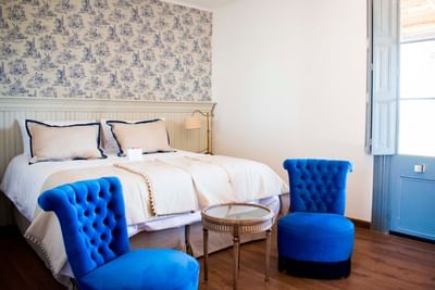 Bedroom with Blue Tufted Chairs,  bed with pillows by blue tufted chairs & a glass table at NOI Blend Colchagua, Chile