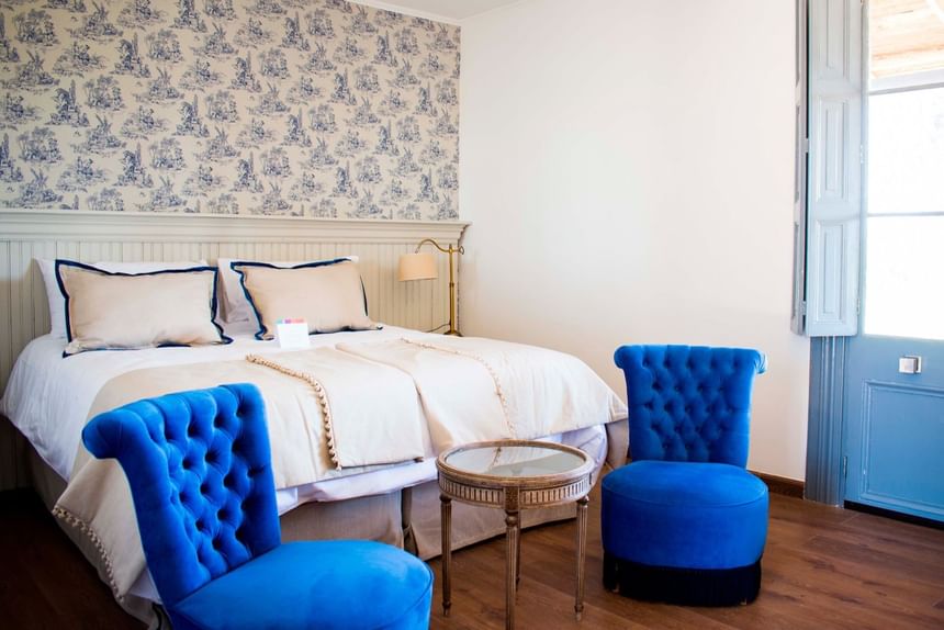 Dormitorio con sillas de mechones azules, cama con almohadas y una mesa de cristal en NOI Blend Colchagua, Chile