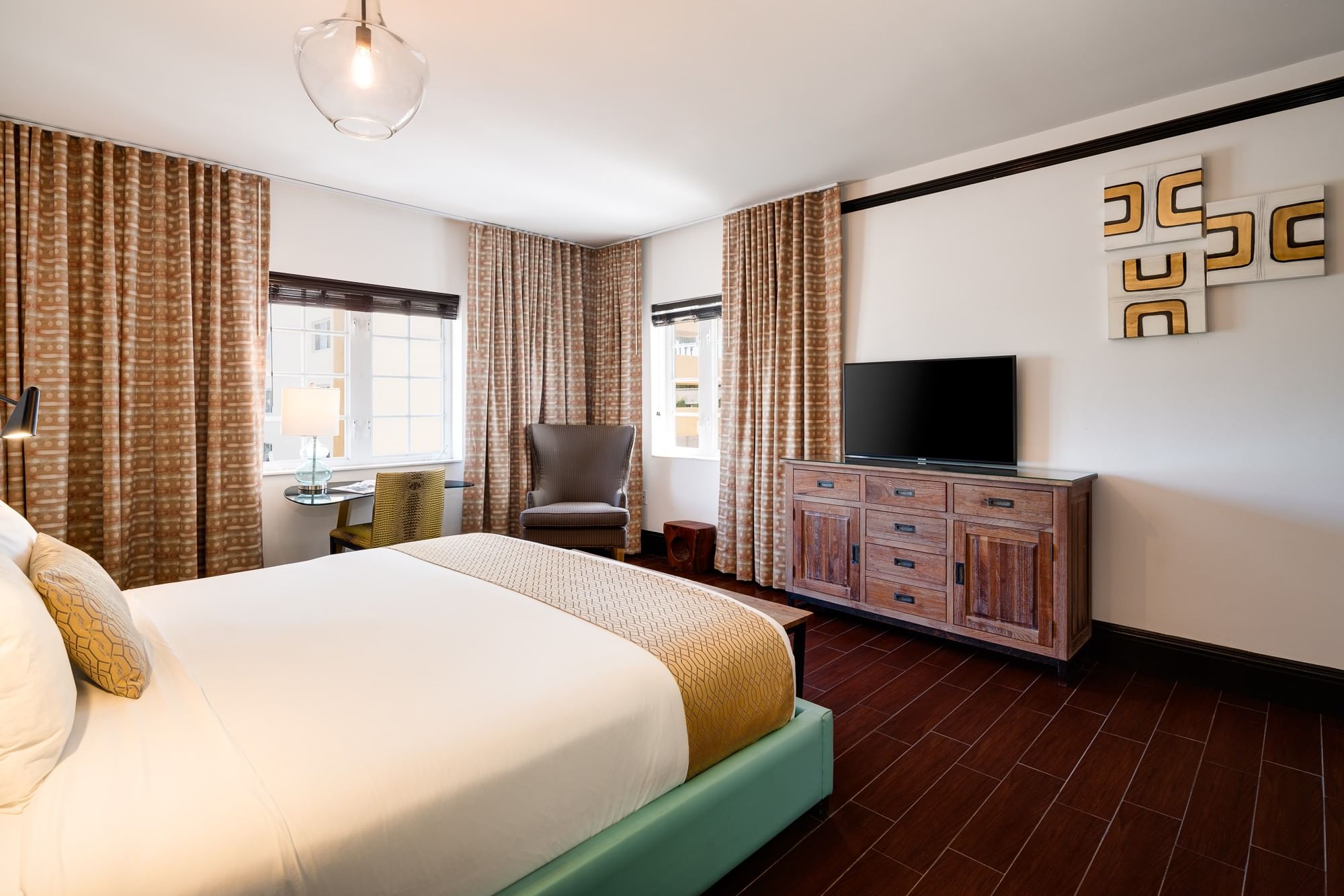 A hotel room with a king-sized bed, TV, chair, desk, and window.