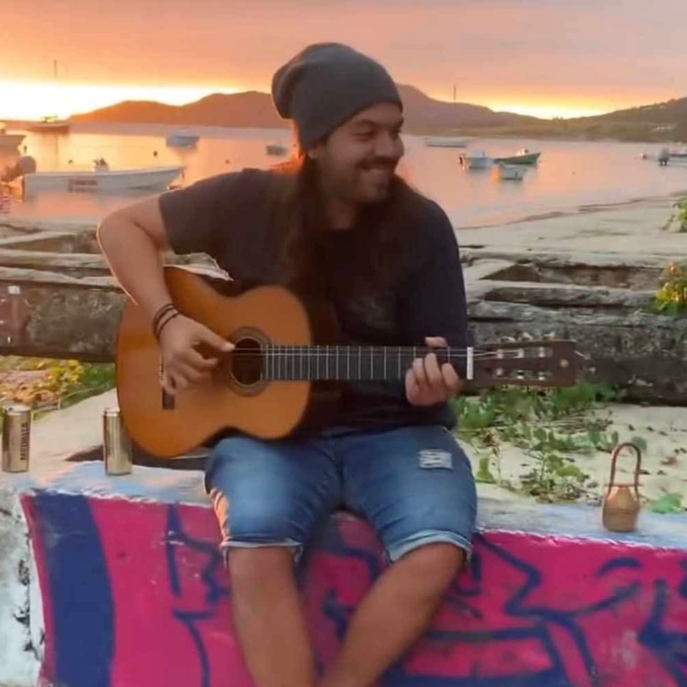 Harold Rivera playing acoustic guitar on colorful mat by waterfront at sunset at El Blok Hotel in Vieques.