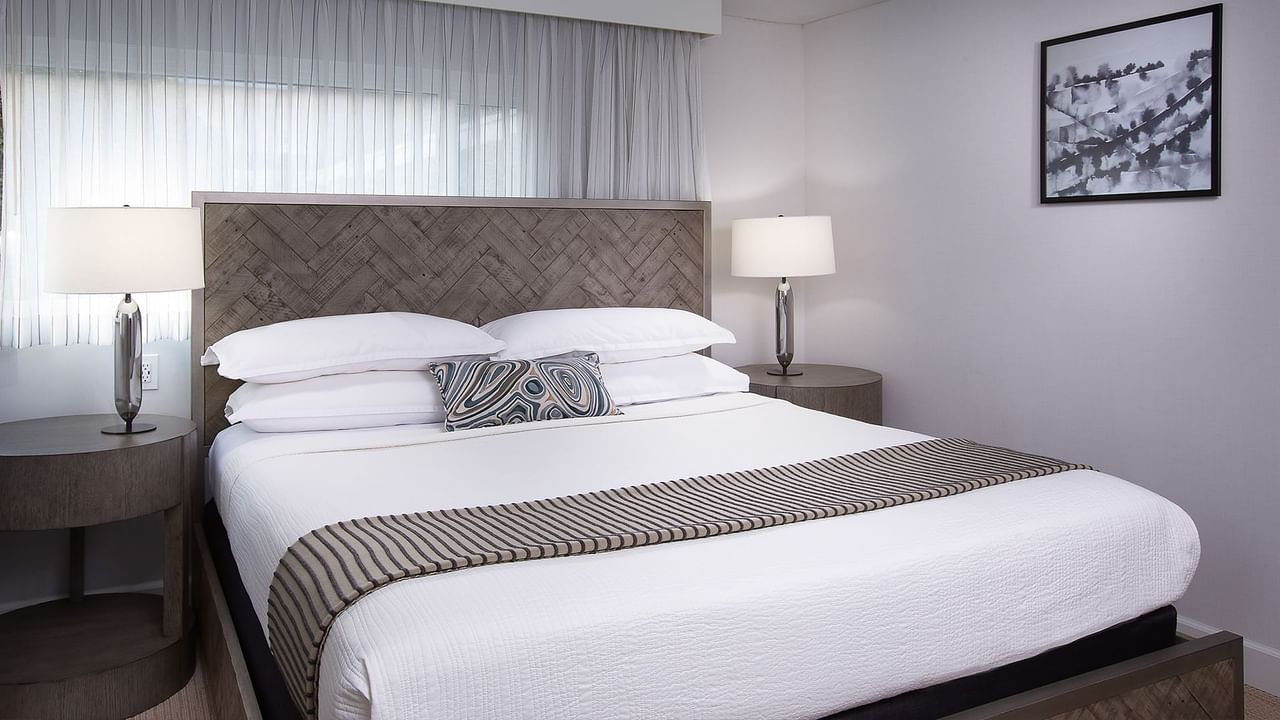 A well-decorated bedroom with a large bed, two nightstands, and a framed picture on the wall.