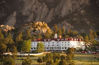A beautiful sunlit view of the historic The Stanley Hotel surrounded by towering mountains and pine trees
