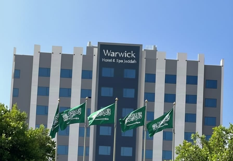 Warwick Jeddah Hotel & Spa entrance with green flags by leafy trees under a clear blue sky 