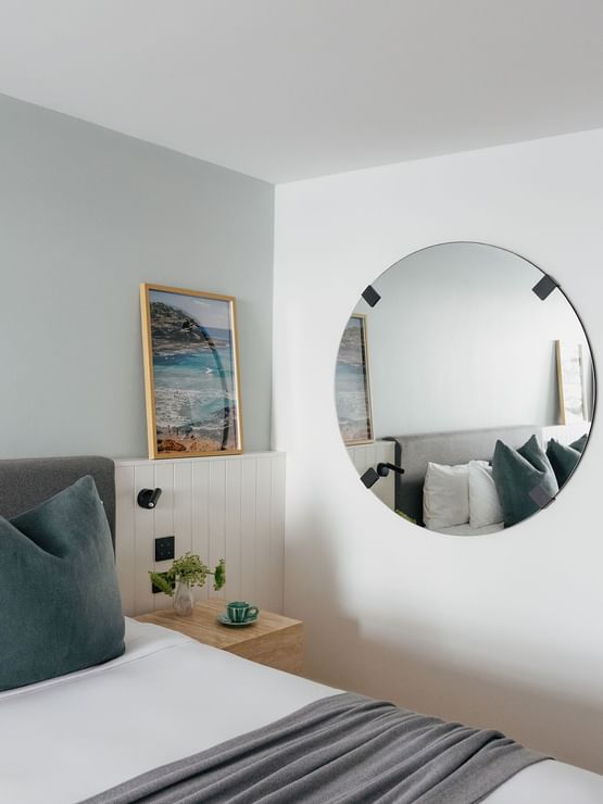 Wellness Suite King at Elysium Hotels with a round mirror by a framed beach print above white wainscoted paneling