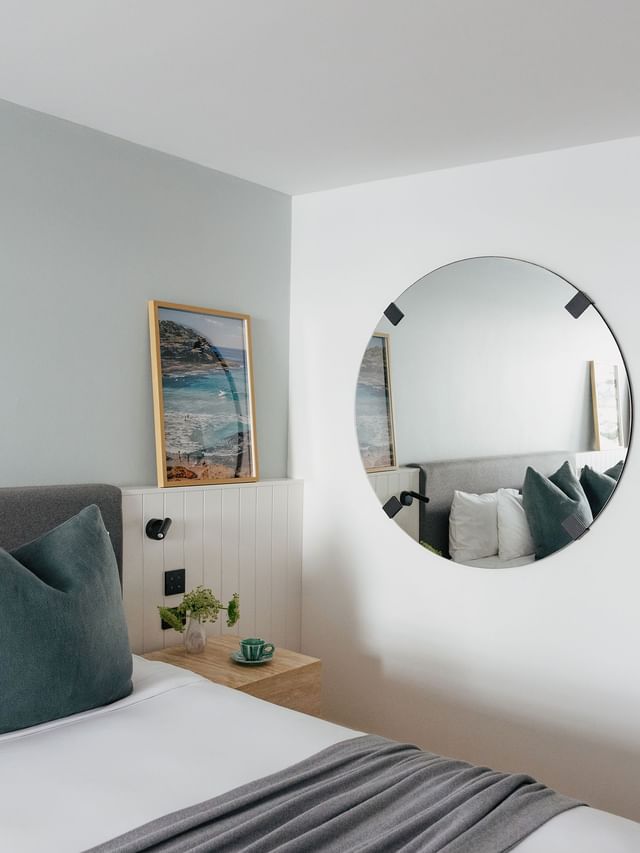 Wellness Suite King at Elysium Hotels with a round mirror by a framed beach print above white wainscoted paneling