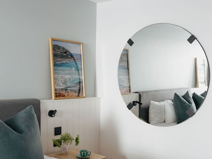 Wellness Suite King at Elysium Hotels with a round mirror by a framed beach print above white wainscoted paneling