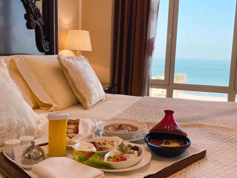 Meal tray on the bed in a room with a sea view at Regency Hotel