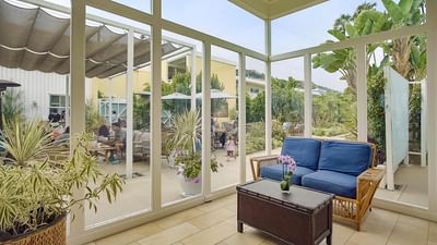 Sunroom with blue sofa and plants, overlooking outdoor patio at Pavilion Hotel Catalina Island