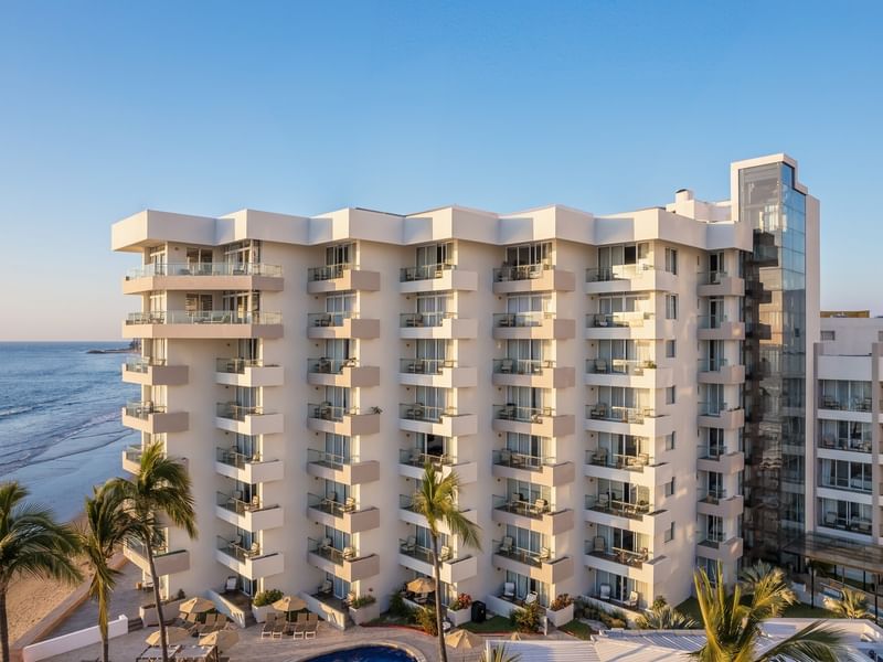 Side view of a modern multi-story Sunvivia Mazatlán beach resort with white balconies located directly on the sandy shoreline