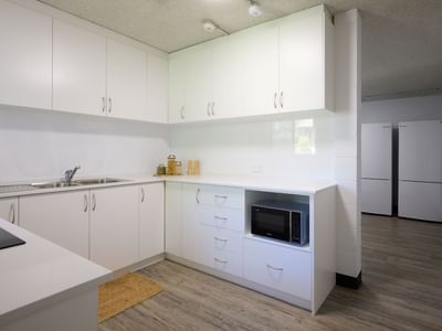 Modern kitchen with white cabinets, sink, microwave, and wooden floors at UniLodge Guild House.