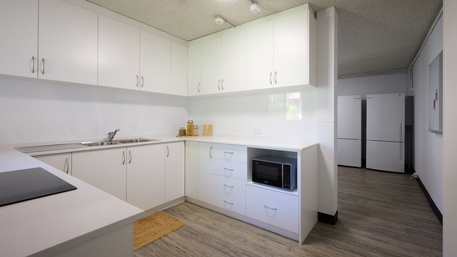 Modern kitchen with white cabinets, sink, microwave, and wooden floors at UniLodge Guild House.