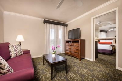 Suite living area with purple sofa, coffee table, TV, and view into bedroom at London Bridge Resort
