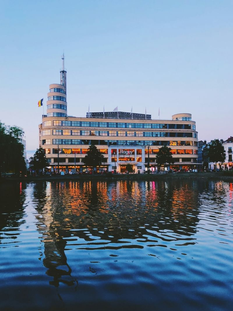 Flagey building with glowing windows by a calm lake reflecting city lights near Hotel Barsey by Warwick
