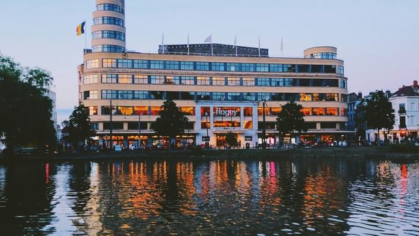 Flagey building with glowing windows by a calm lake reflecting city lights near Hotel Barsey by Warwick