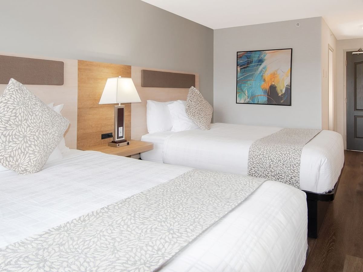 Hotel room with two queen beds, bedside table lamp, and art on the wall