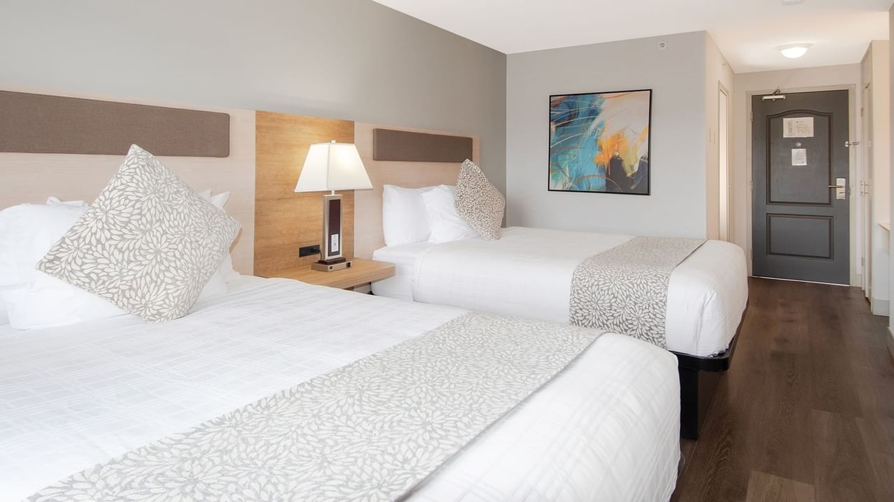 Hotel room with two queen beds, bedside table lamp, and art on the wall