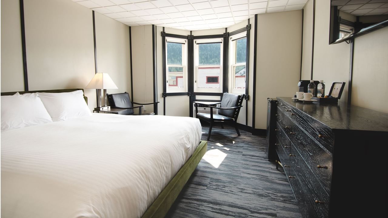 Hotel room with king bed, lamp, night stand, premium coffee, TV, chair, and window