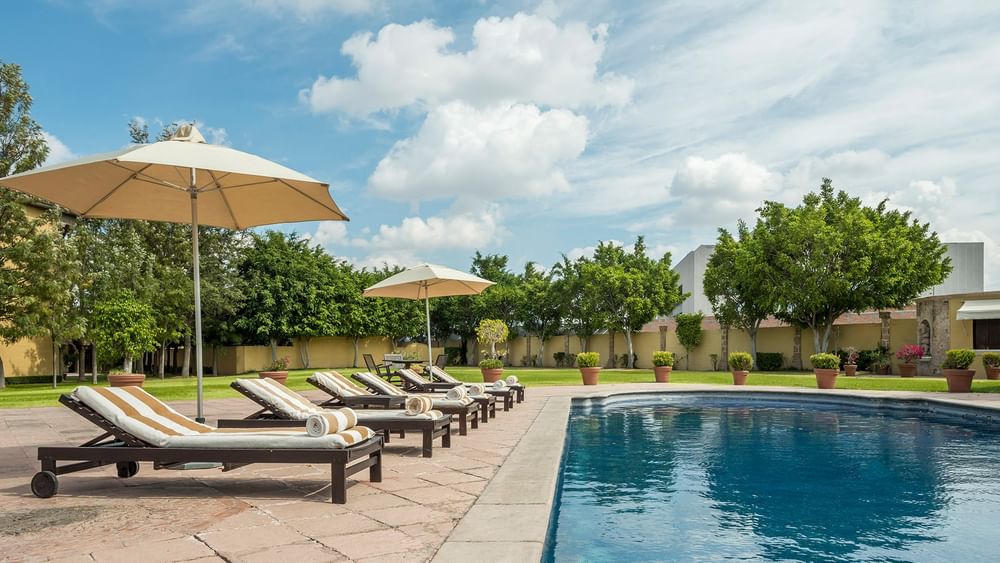 Striped lounge chairs and umbrellas by a sparkling blue pool at Quinta Real Aguascalientes