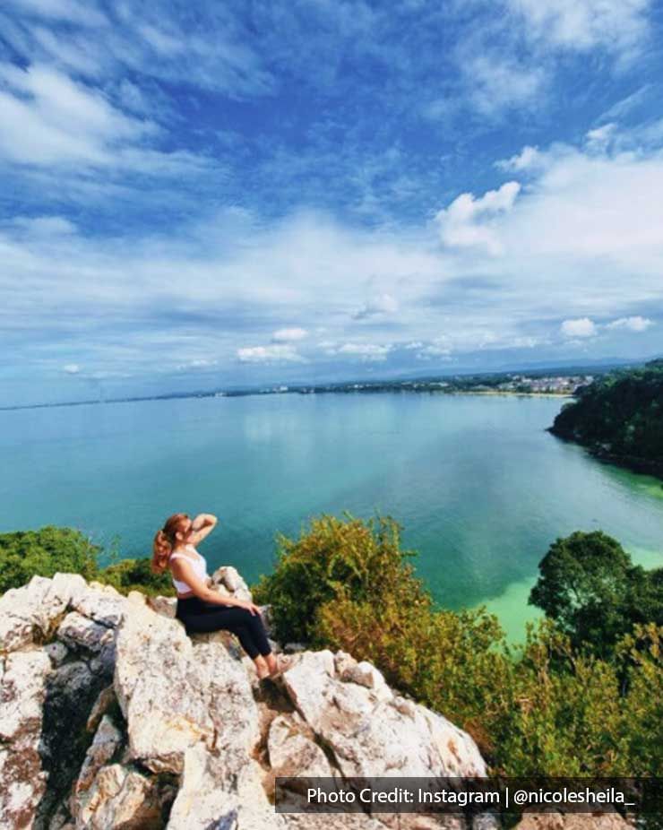 a girl sitting on a rock and taking pictures with the ocean at the back