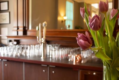 Bouquet of pink tulips in a vase by a long wooden bar counter under soft lighting at Rodd Charlottetown Hotel