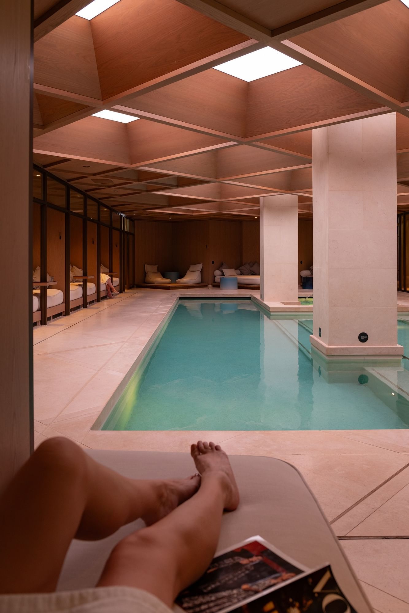 People relaxing on the comfy beds by the indoor pool at The Londoner Hotel