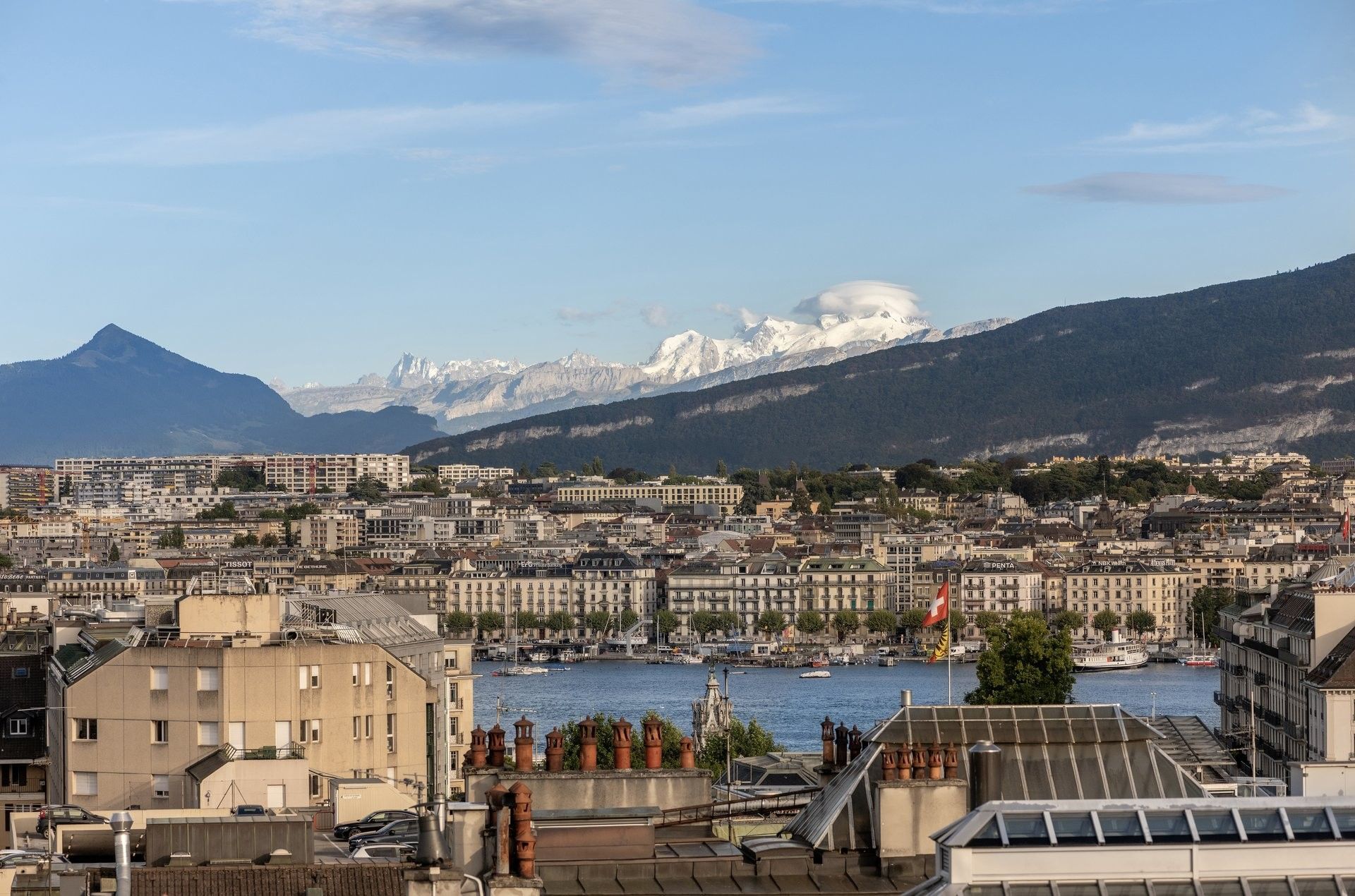 City buildings by a blue lake under snow-capped mountains near Warwick Geneva