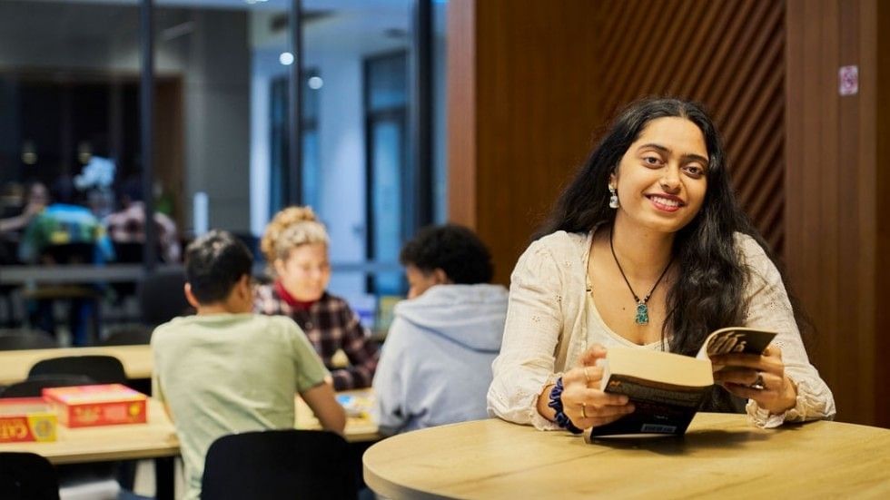A resident reads a book at a table in a study area with other students at UniLodge.