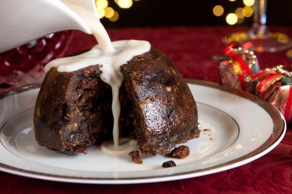 Someone pouring cream over christmas pudding