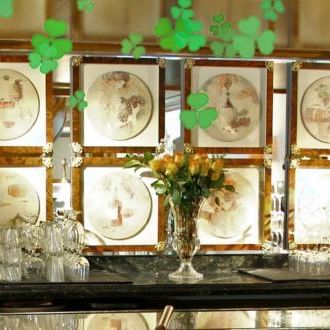 Bar counter with glasses and a floral centerpiece, featuring a decorative wall of plates at The Rose Hotel