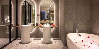 Stylish modern bathroom featuring marble sinks, a soaking tub with rose petals, and elegant lighting at One World Hotel