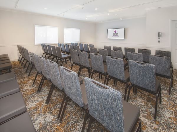 Rows of chairs in a meeting room with a screen and carpeted floor.