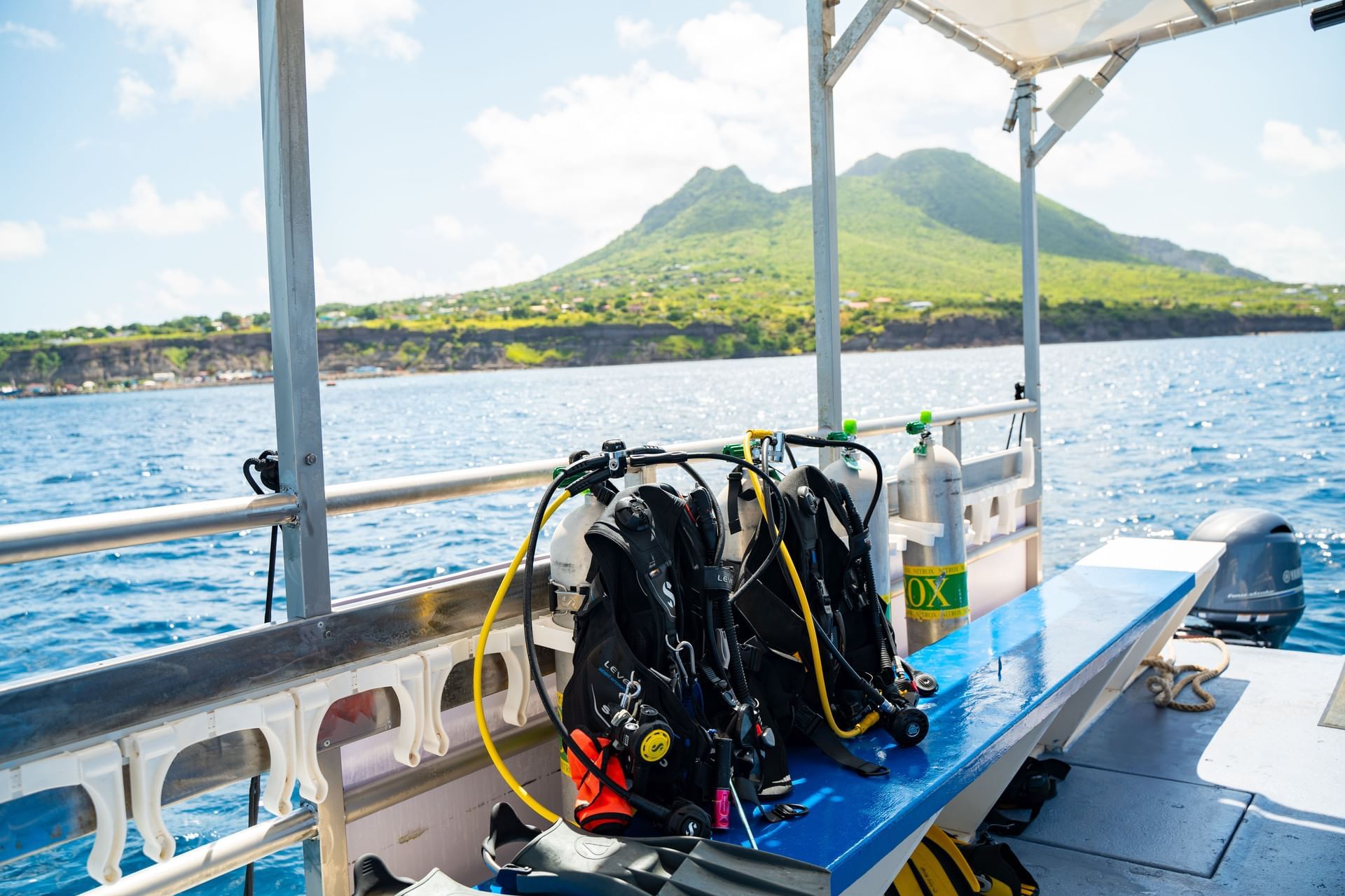 Scuba diving equipment with air tanks on a dive boat near the tropical island coast with a volcano at Golden Rock Resort