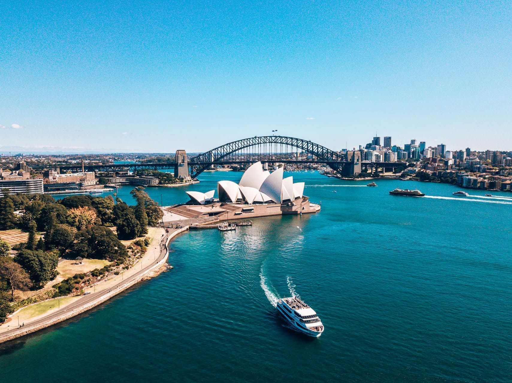 Aerial view of Sydney Opera House and Harbour Bridge with boats and cityscape in the background.