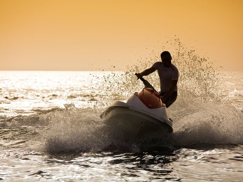 A man riding a jet ski at sunset on the beach near Ajman Hotel