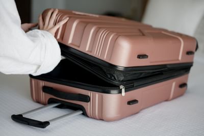 Guest opening a hard-shell suitcase on a white bed sheet at La Tourelle Hotel and Spa