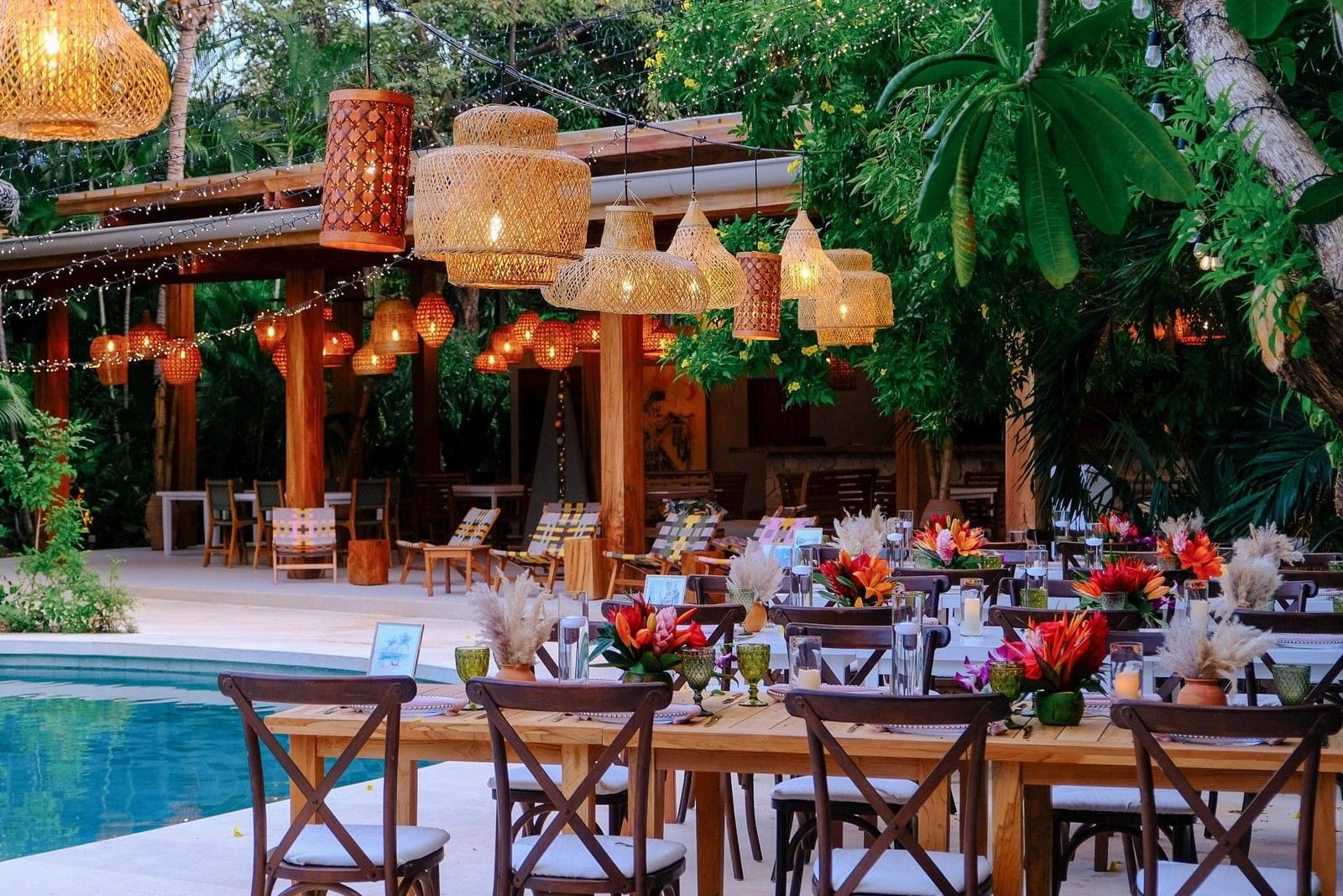 Set outdoor dining area by a pool with tropical decor and hanging lights at Cala Luna Boutique Hotel