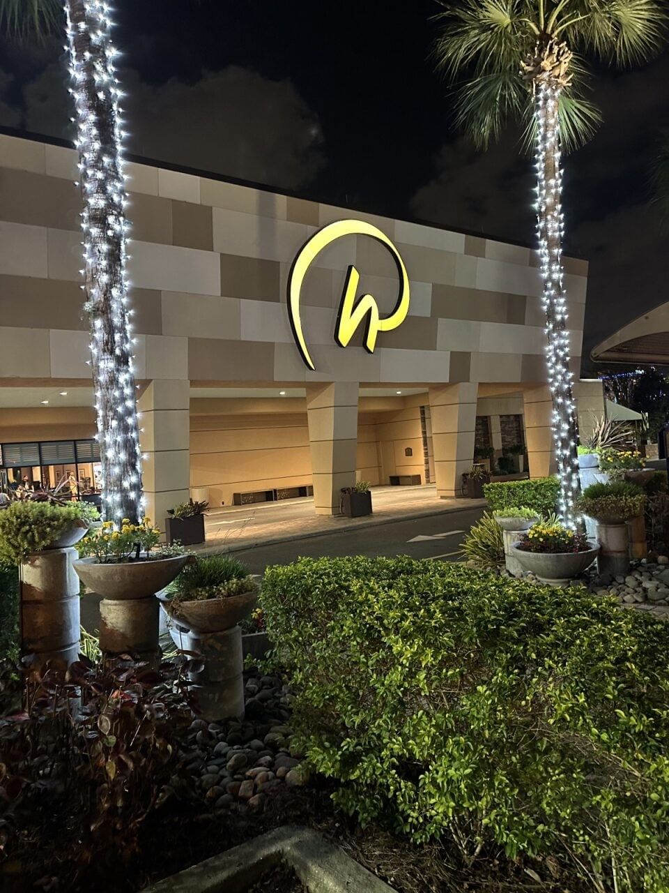 The front entrance to Rosen Inn International at night, flanked by two palm trees wrapped in white Christmas lights. 